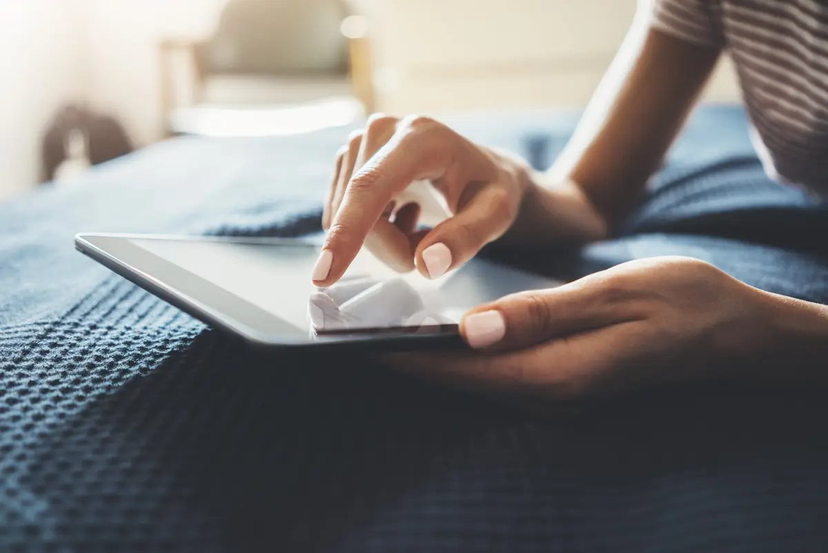 Une personne posée sur son lit navigue sur sa tablette