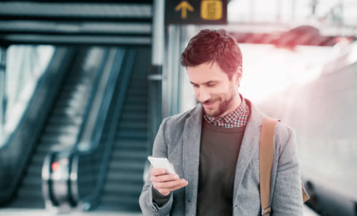 A man at an airport, looking at his phone and smiling, with a focus on cloud access security solutions.