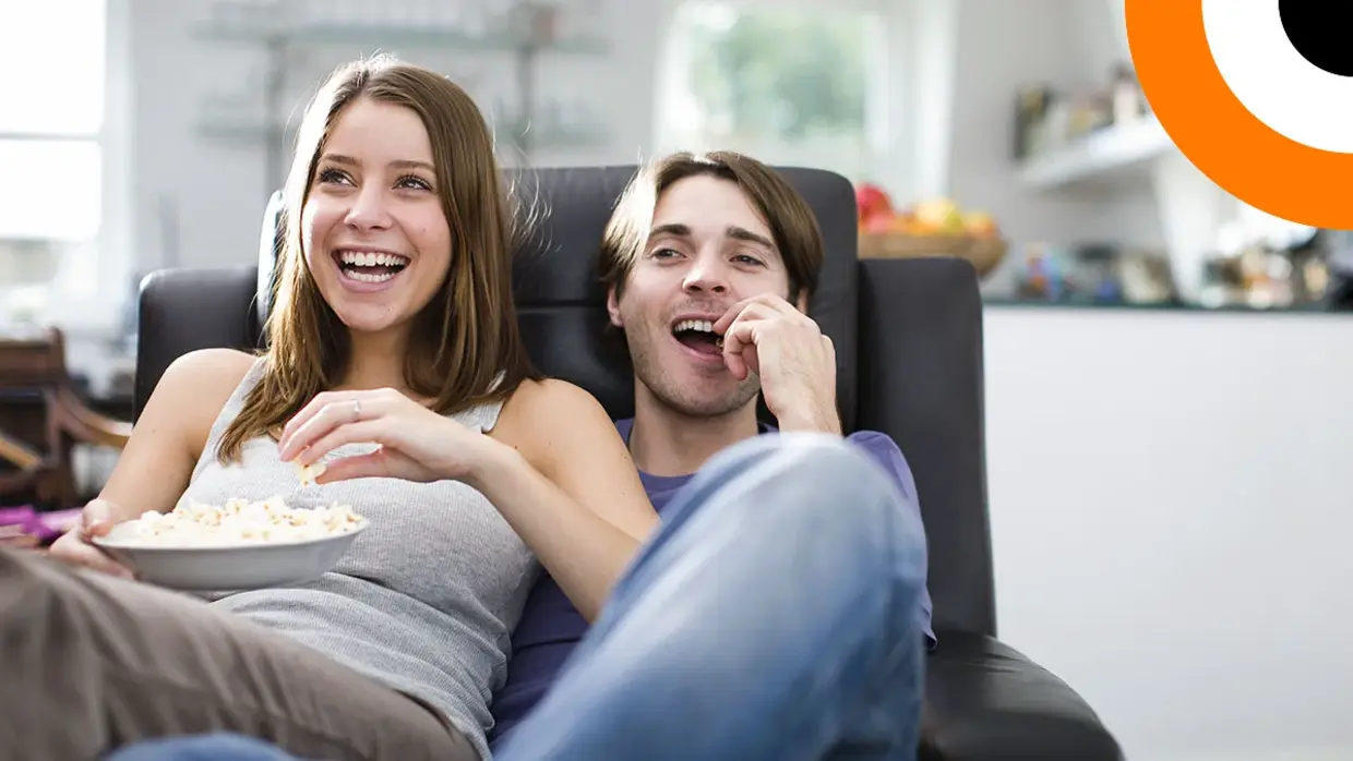 Quand la cybersécurité tisse sa toile sur le grand et le petit écran Un couple assis sur un canapé consomme du pop corn en regardant un film.