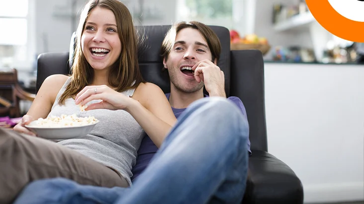 Quand la cybersécurité tisse sa toile sur le grand et le petit écran Un couple assis sur un canapé consomme du pop corn en regardant un film.