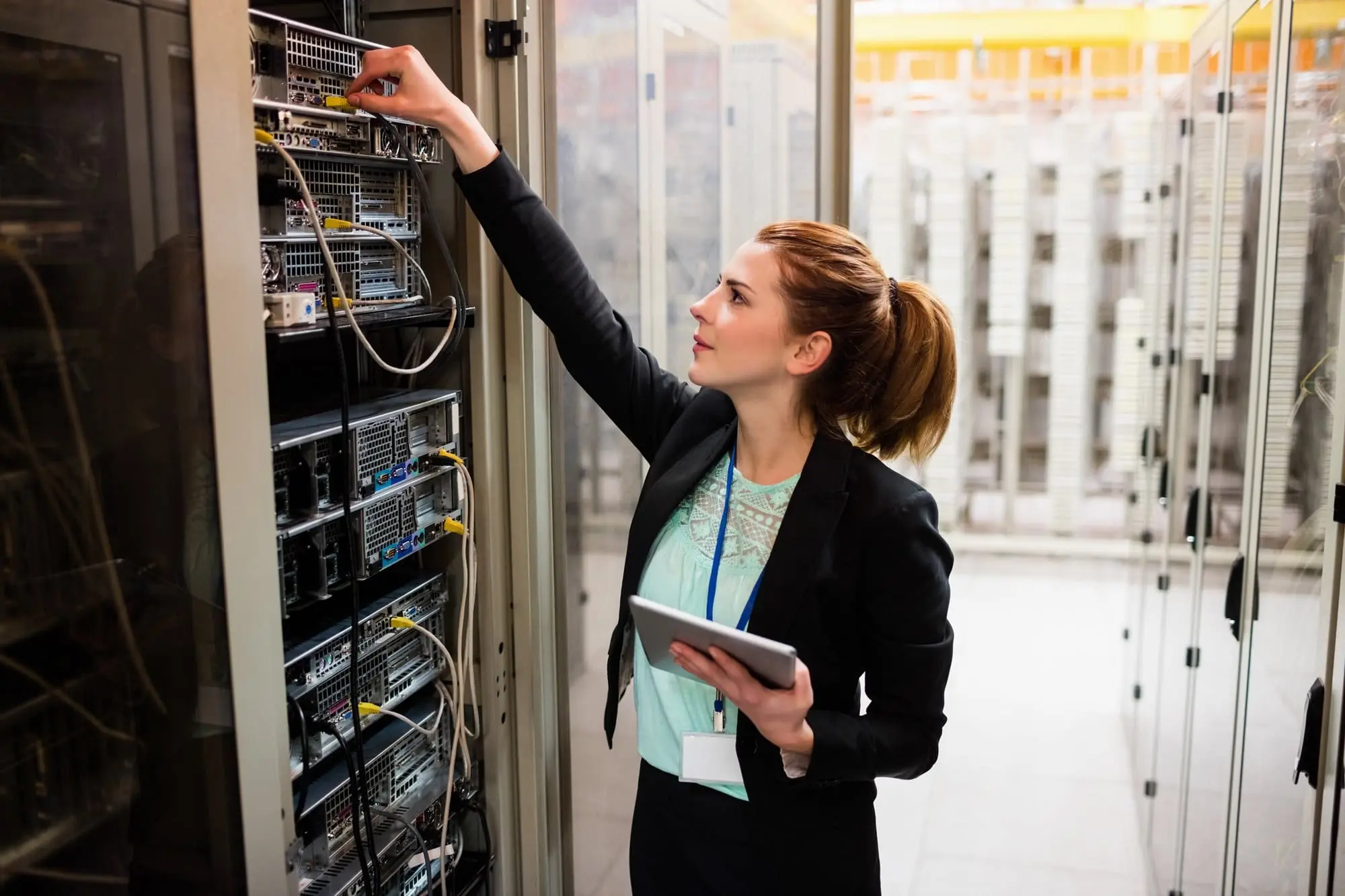 A woman working in a data center, adjusting network equipment in a server rack.