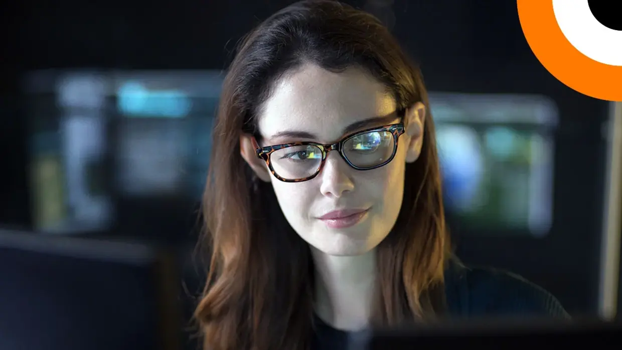 Quels sont les risques du Shadow IT et du Shadow AI ? Une jeune femme portant une paire de lunettes, travaillant dans une salle informatique regarde un écran d'ordinateur.