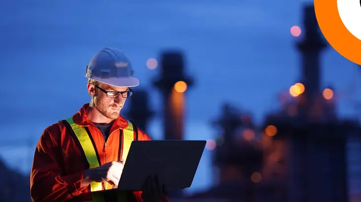 Les enjeux de la directive NIS 2, entre mise en conformité et résilience des entreprises européennes. Un homme vêtu d'une combinaison et d'un casque industriel consulte un ordinateur portable à la nuit tombée.