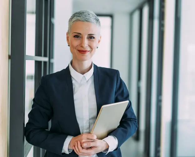 "Smiling businesswoman in a suit holding a tablet in an office