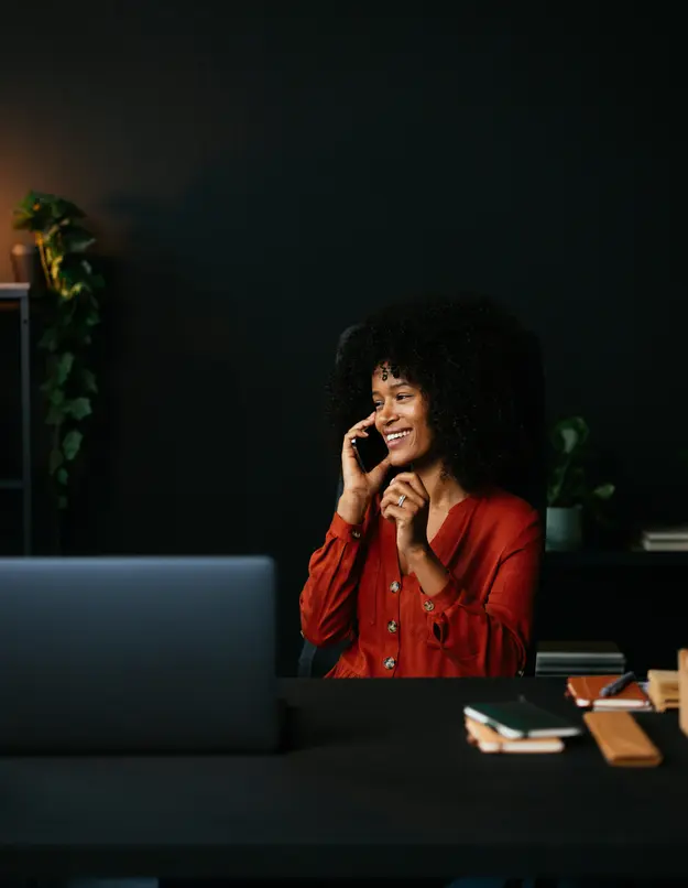 Smiling woman on a phone call at her desk in a dark office