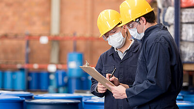Two workers wearing hardhats and overalls looking at a clipboard at a industrial site