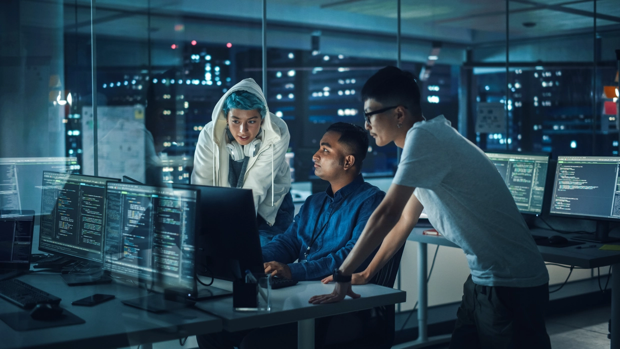 Three team members huddled around a screen in a server room environment