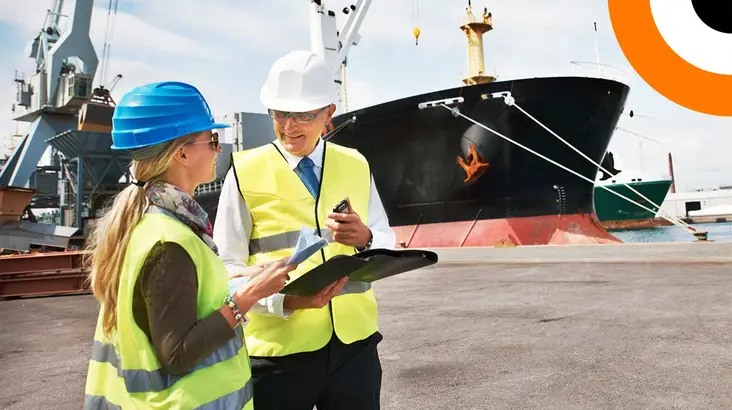 Cybersécurité des sites industriels : le panorama des menaces Deux professionnels portant un gilet jaune se consultent l'un l'autre avec en toile de fond un bateau de transport maritime.