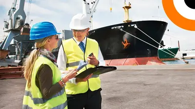Cybersécurité des sites industriels : le panorama des menaces Deux professionnels portant un gilet jaune se consultent l'un l'autre avec en toile de fond un bateau de transport maritime.