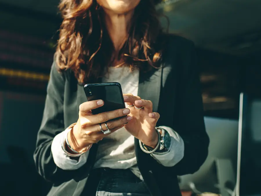 Une femme en tailleur qui sourit et qui consulte son mobile
