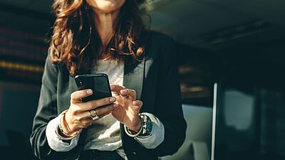 Une femme en tailleur qui sourit et qui consulte son mobile