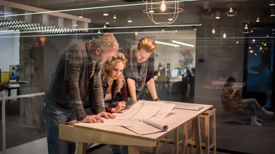 Three team members standing at a table reviewing blueprints