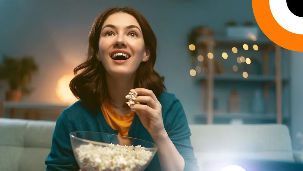 Quand la cybersécurité fait son intrusion au cinéma, épisode 1 Une jeune femme mange du pop corn en regardant un film avec son vidéoprojecteur, avec un air enthousiaste.