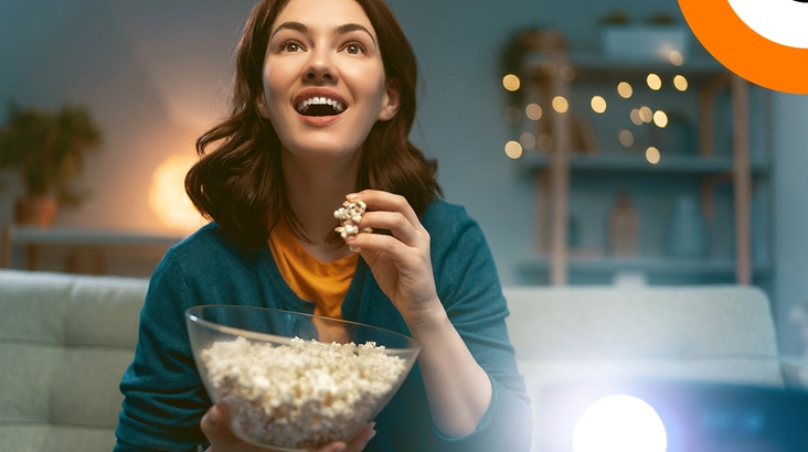 Quand la cybersécurité fait son intrusion au cinéma, épisode 1 Une jeune femme mange du pop corn en regardant un film avec son vidéoprojecteur, avec un air enthousiaste.