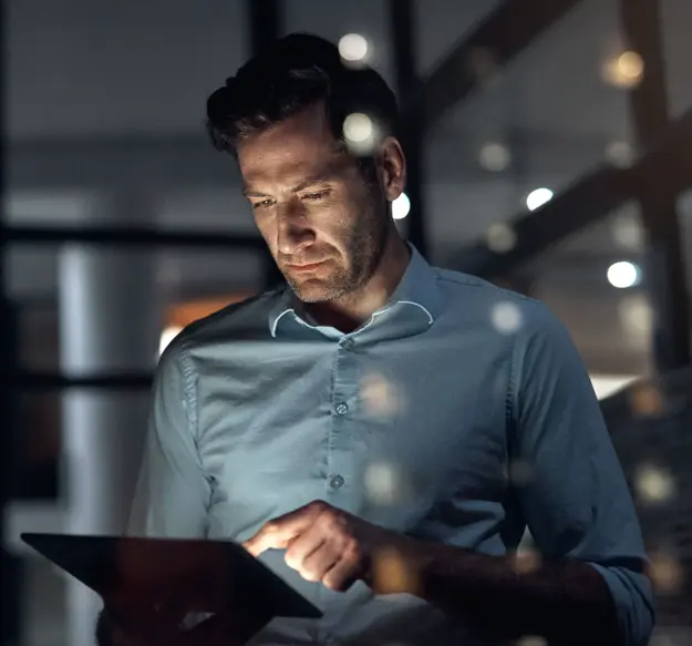 Focused professional working on a tablet in a dark office at night