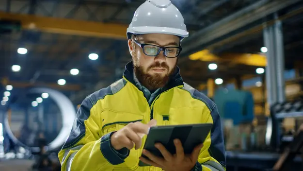 Engineer using a tablet on a factory floor, representing connected industrial systems protected by OT security