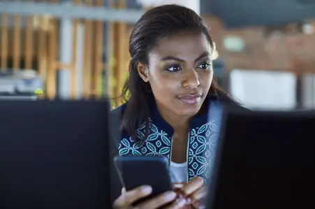 Une femme consulte un message sur son mobile et regarde son écran d'ordinateur