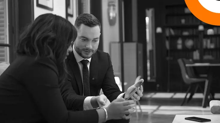 dora_mise_en_conformite_entreprises Un homme et une femme bien habillés sont assis côte à côte et regardent une tablette.