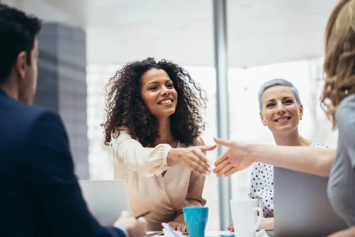 A diverse team in a meeting, smiling and shaking hands, with a focus on cloud security strategy and compliance.